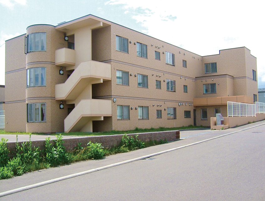 3階建ての介護施設の建物外観。レンガ造りで階段状のバルコニーが特徴的