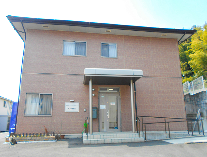 赤茶色レンガ造りの介護施設の玄関。モダンな庇と段差のないアプローチが特徴。