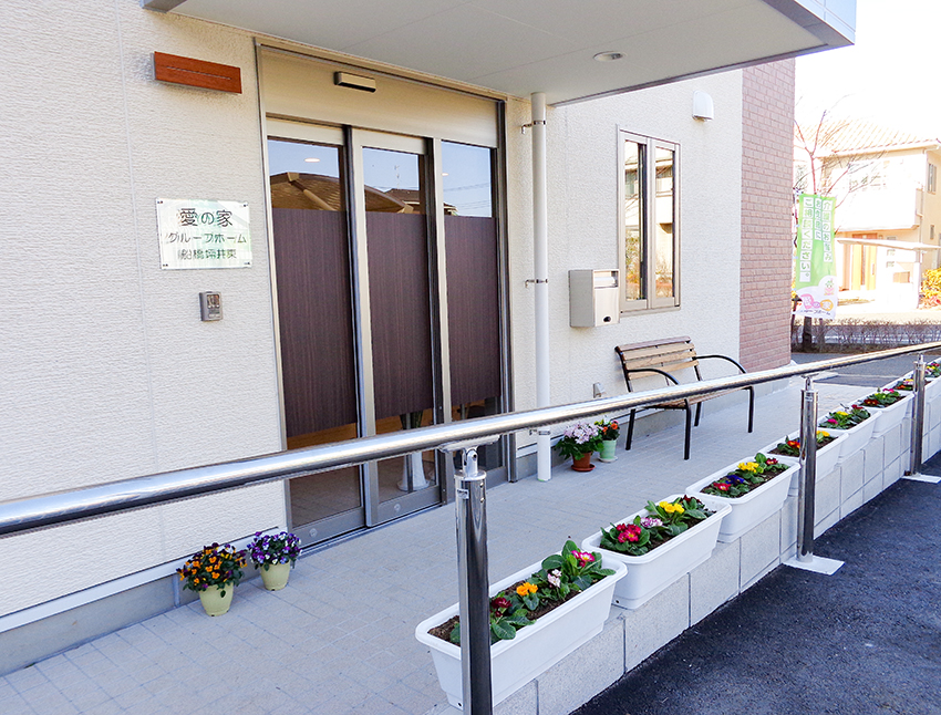 施設玄関の車寄せエリア。花壇と手すりが備えられた安全な出入り空間。