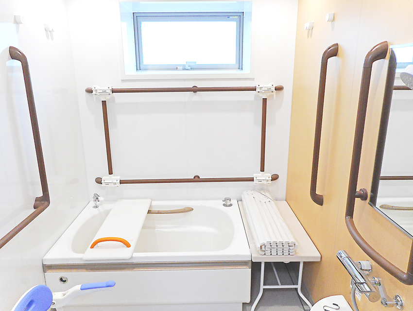 介護浴室。白い浴槽に茶色い手すりと昇降機が装備されている。