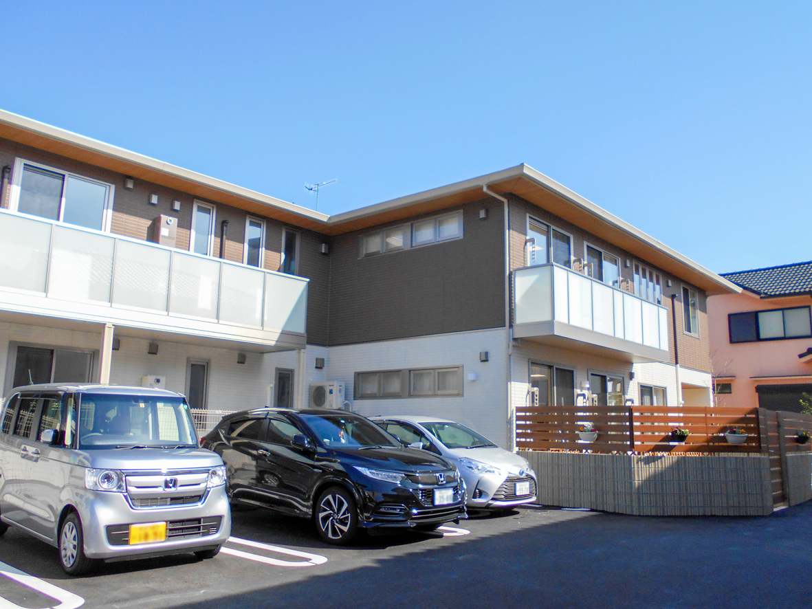 介護施設の建物外観。駐車場に複数の車が停まっており、モダンな平屋建て施設が見える。