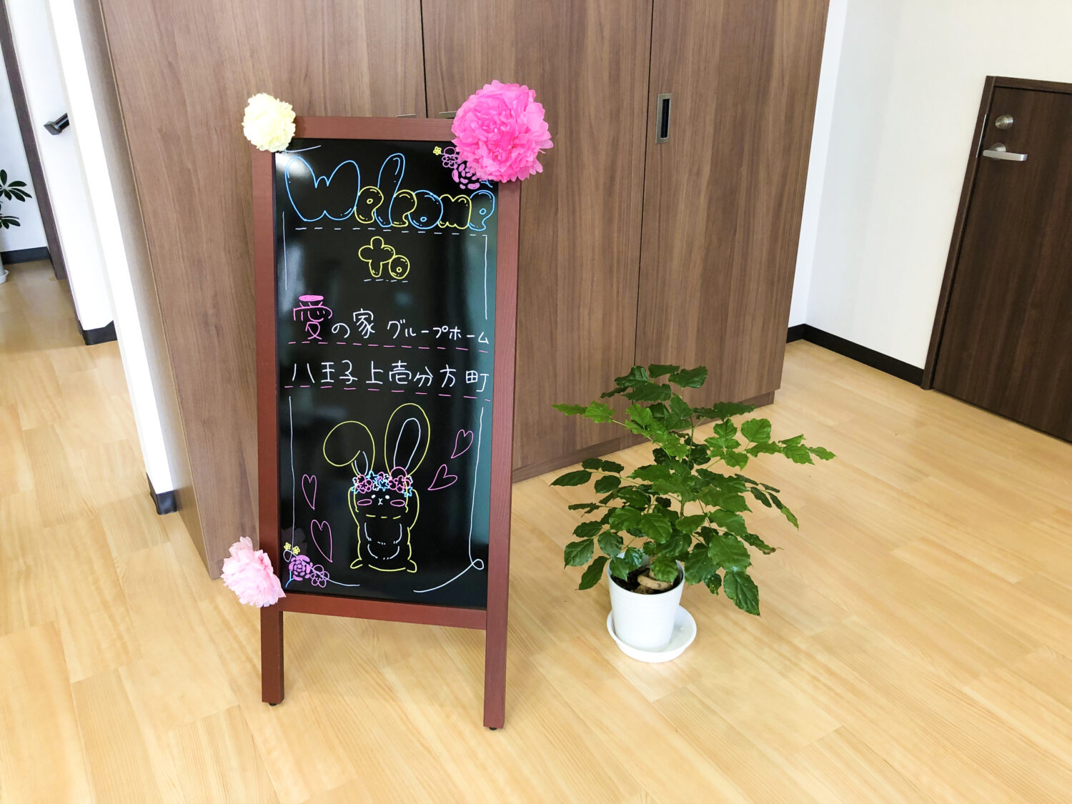 施設内ロビーのウェルカムボード。チョークアート装飾と観葉植物で親しみやすい雰囲気