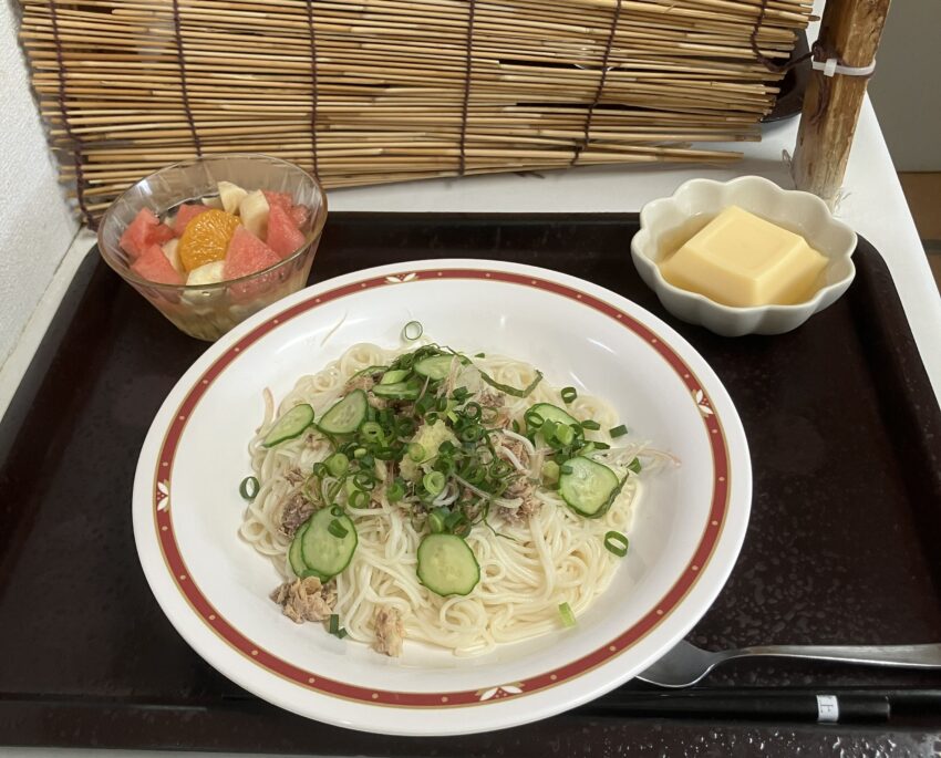 介護施設の食事風景。冷麺と果物、バターが黒いトレーに盛り付けられている。
